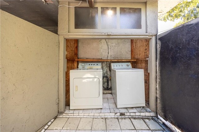 clothes washing area with a textured wall, washer and clothes dryer, and laundry area