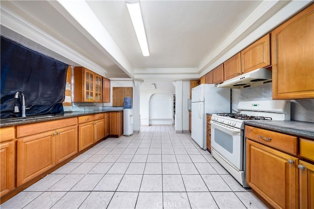 kitchen with brown cabinetry, glass insert cabinets, under cabinet range hood, and white appliances