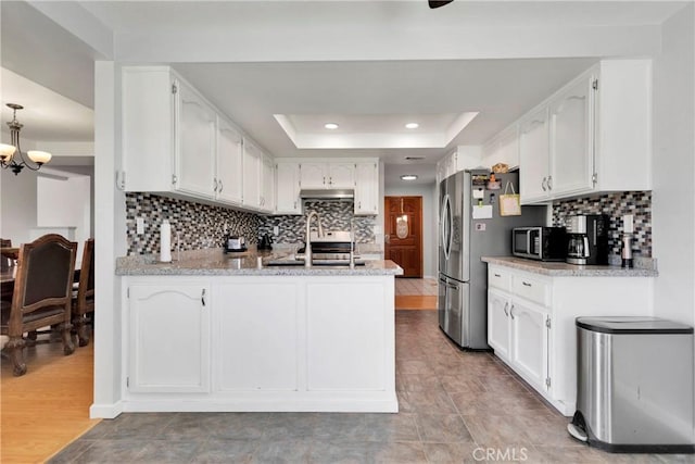 kitchen with white cabinetry, a tray ceiling, stainless steel appliances, a sink, and a peninsula