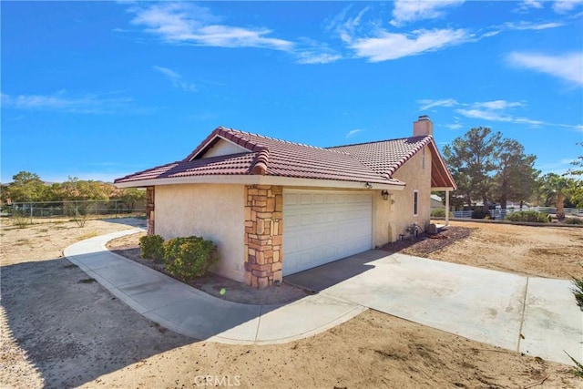 view of home's exterior featuring fence, a tiled roof, a chimney, an attached garage, and stucco siding
