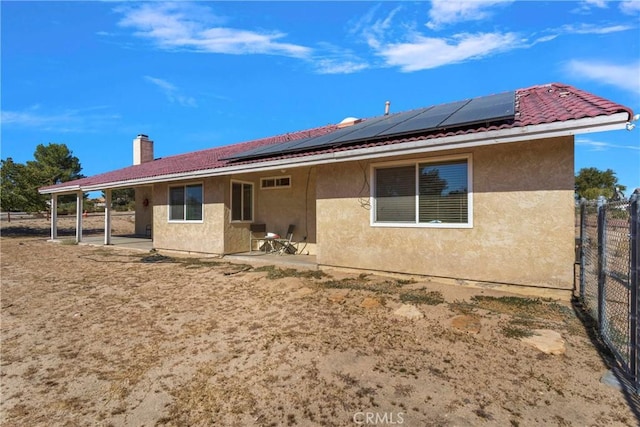 back of house with stucco siding, a tiled roof, solar panels, and a patio area