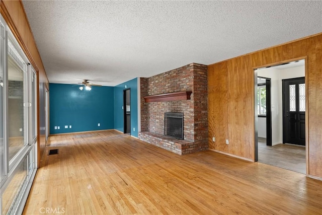 unfurnished living room featuring wood finished floors, a brick fireplace, wood walls, and visible vents