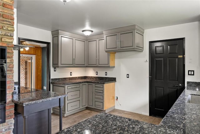 kitchen with gray cabinetry, black electric cooktop, a sink, and dark stone counters