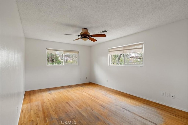 empty room with visible vents, a ceiling fan, wood finished floors, and a healthy amount of sunlight