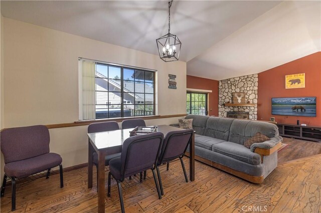 dining space featuring an inviting chandelier, wood-type flooring, a stone fireplace, baseboards, and lofted ceiling