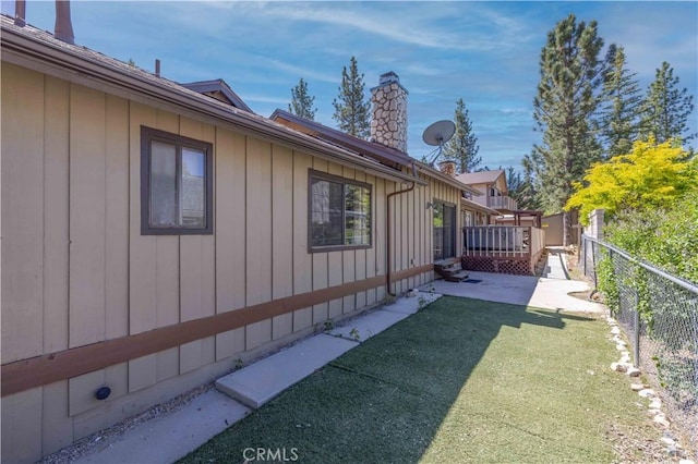 view of home's exterior featuring a chimney, a deck, a fenced backyard, a yard, and a patio