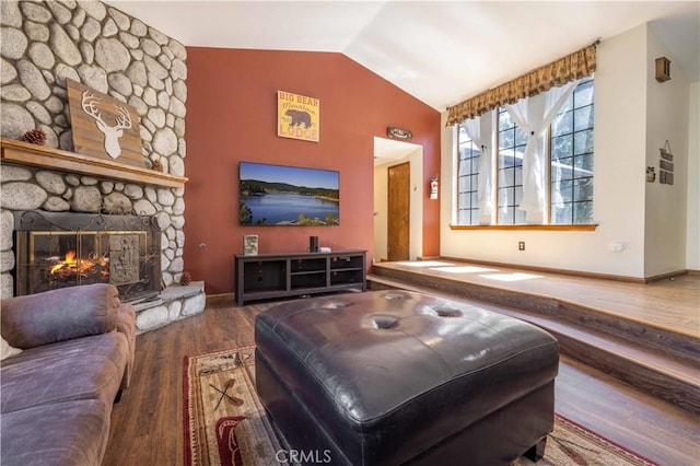 living room with baseboards, a stone fireplace, vaulted ceiling, and wood finished floors