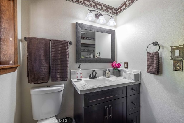 bathroom with vanity, a textured wall, and toilet