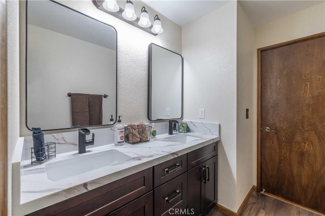 full bathroom featuring a sink, a textured wall, double vanity, and wood finished floors