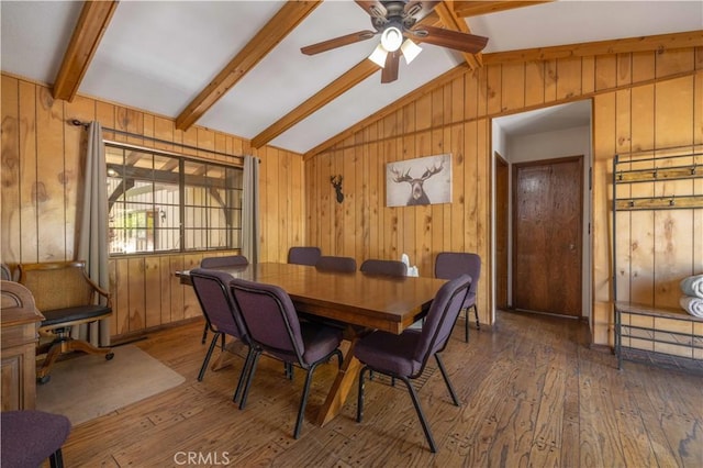 dining space with vaulted ceiling with beams, ceiling fan, wood finished floors, and wooden walls