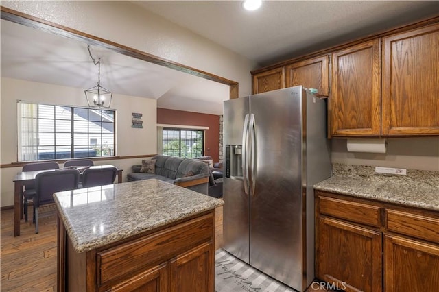 kitchen featuring brown cabinets, stainless steel fridge, light wood finished floors, a center island, and open floor plan