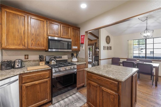 kitchen with appliances with stainless steel finishes, brown cabinetry, light wood-style flooring, and a chandelier