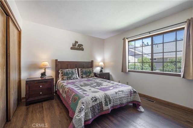 bedroom with dark wood-type flooring, baseboards, visible vents, and a closet