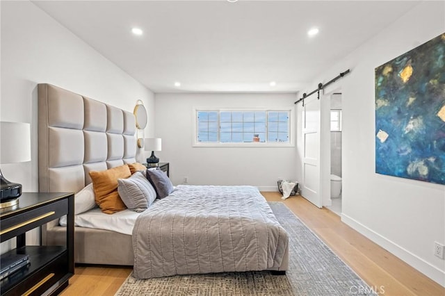 bedroom with baseboards, a barn door, multiple windows, and light wood finished floors