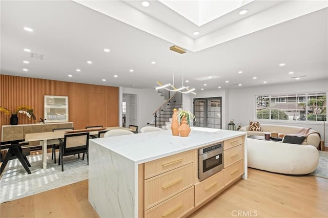 kitchen with light wood finished floors, open floor plan, a center island, and light brown cabinets