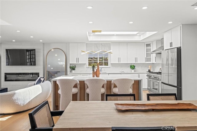 kitchen featuring white cabinetry, light countertops, a center island, wall chimney range hood, and appliances with stainless steel finishes