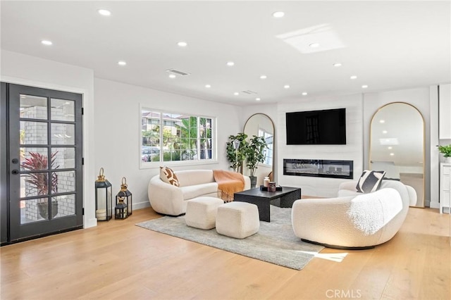 living room with arched walkways, recessed lighting, light wood-style flooring, and a glass covered fireplace