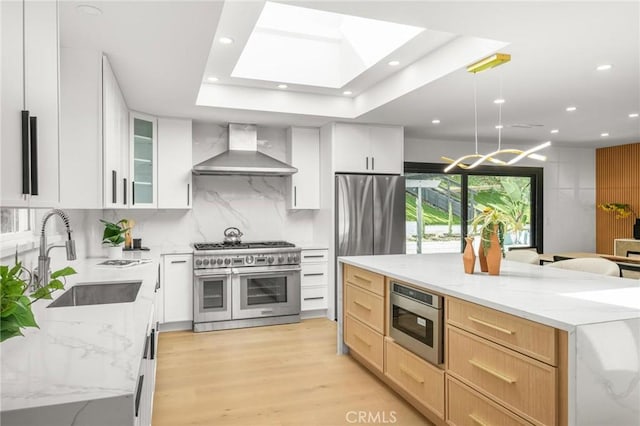 kitchen featuring tasteful backsplash, stainless steel appliances, a sink, a skylight, and wall chimney range hood