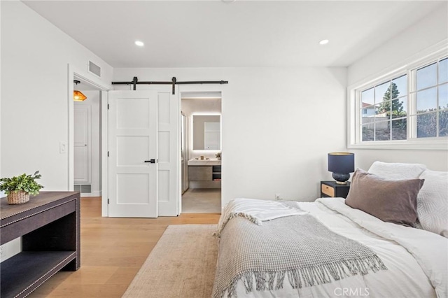 bedroom with light wood-style flooring, visible vents, a barn door, and recessed lighting