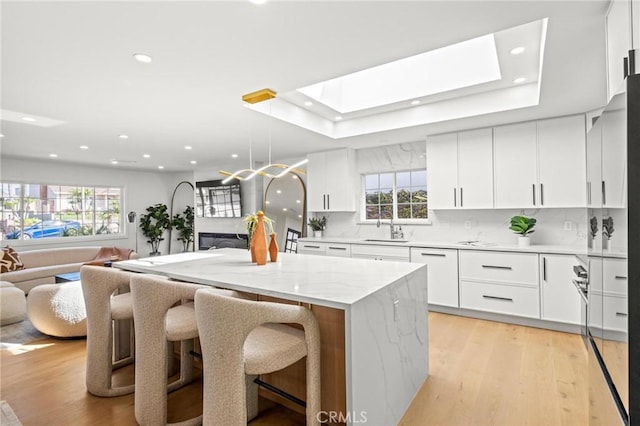 kitchen featuring open floor plan, a kitchen island, a skylight, and light wood finished floors