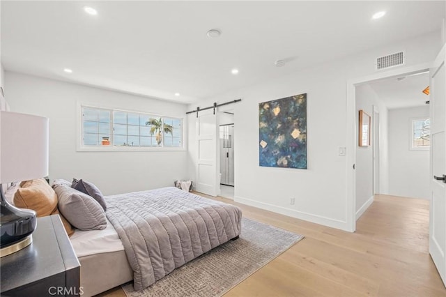 bedroom with a barn door, light wood-type flooring, baseboards, visible vents, and recessed lighting