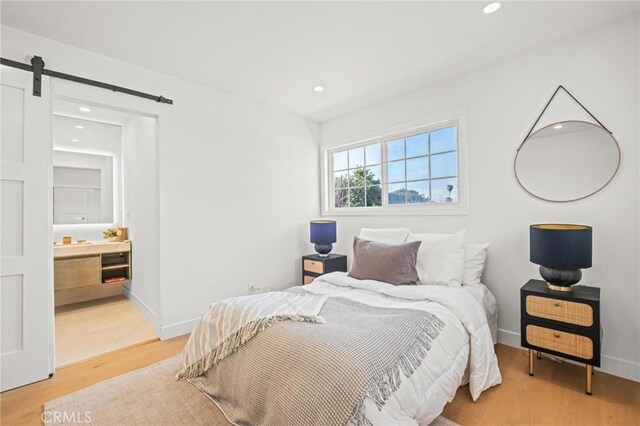 bedroom with light wood-style flooring, baseboards, a barn door, and recessed lighting