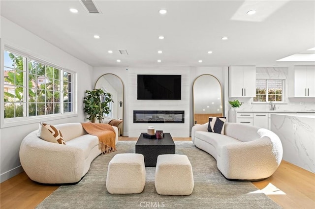 living room featuring light wood finished floors, a large fireplace, baseboards, visible vents, and recessed lighting