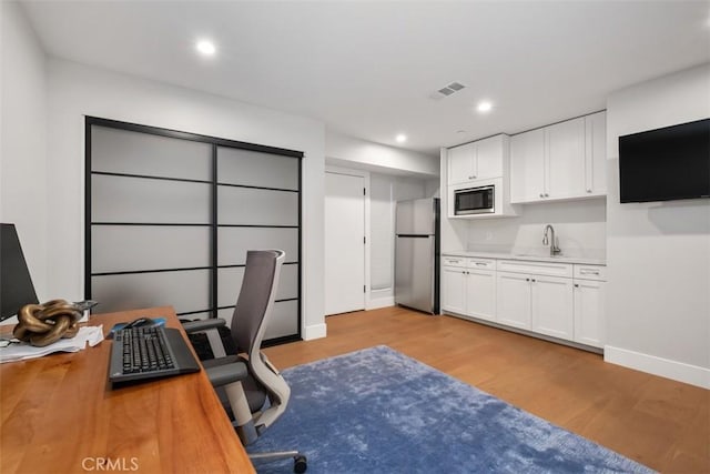 home office with visible vents, light wood finished floors, baseboards, recessed lighting, and a sink