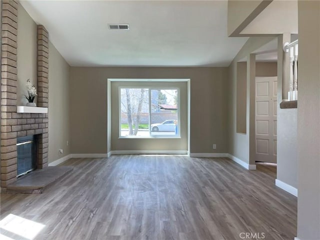 unfurnished living room with baseboards, wood finished floors, and a brick fireplace
