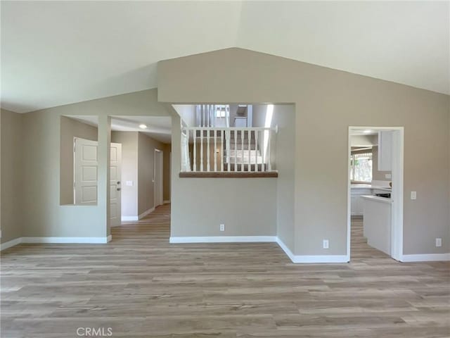 unfurnished living room with vaulted ceiling, baseboards, and light wood-style floors