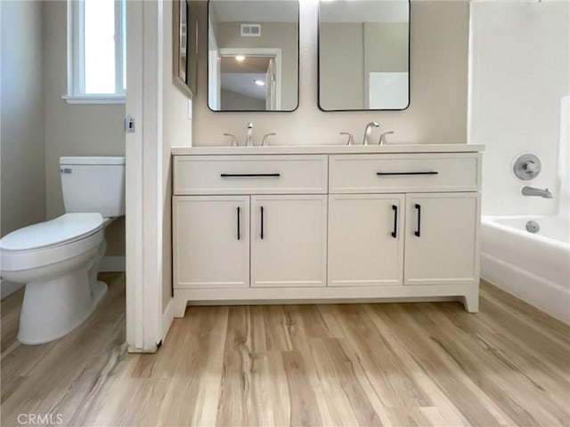 full bath with toilet, wood finished floors, a tub to relax in, double vanity, and baseboards