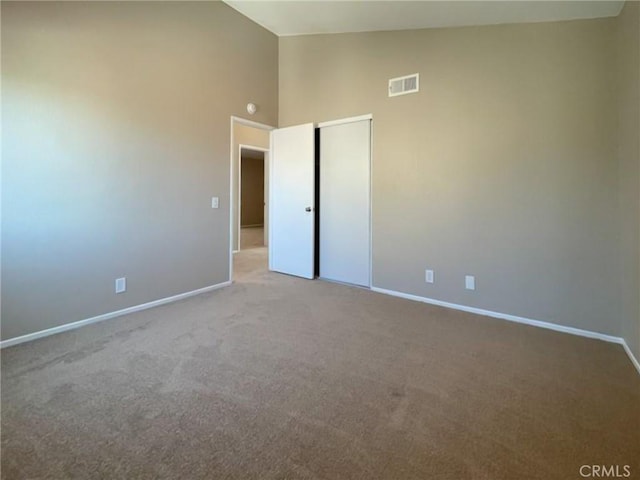 empty room featuring baseboards, carpet flooring, and high vaulted ceiling