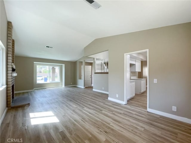 unfurnished living room with light wood finished floors, baseboards, and vaulted ceiling