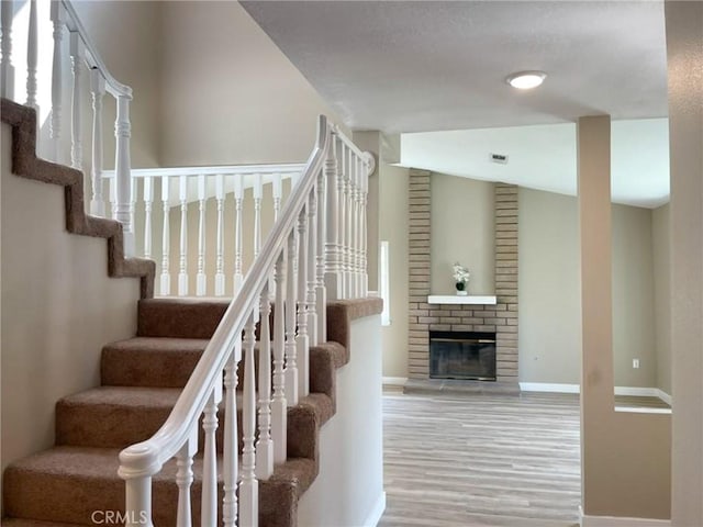 stairs featuring wood finished floors, baseboards, and a brick fireplace