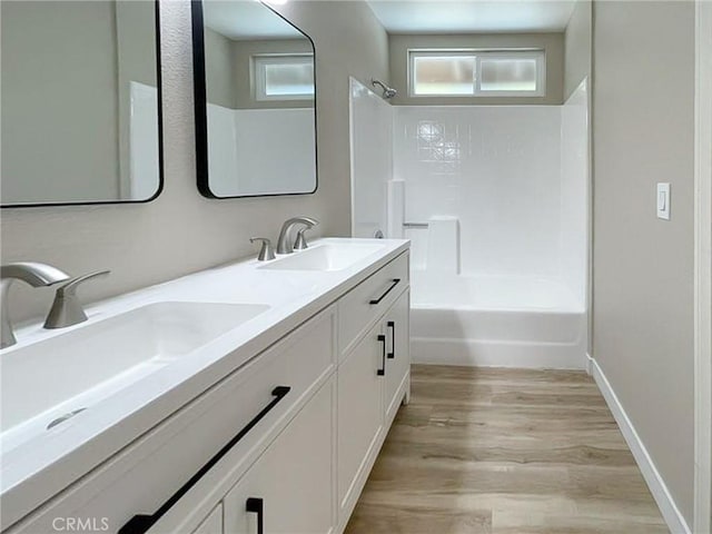 bathroom with wood finished floors, shower / washtub combination, double vanity, and baseboards