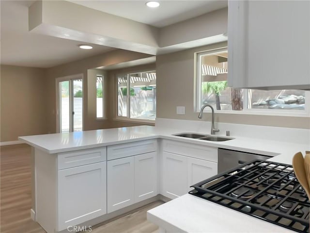 kitchen featuring a sink, a peninsula, light countertops, white cabinets, and light wood finished floors