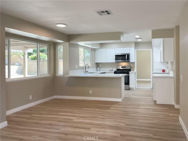 kitchen with appliances with stainless steel finishes, baseboards, white cabinetry, light wood finished floors, and a sink