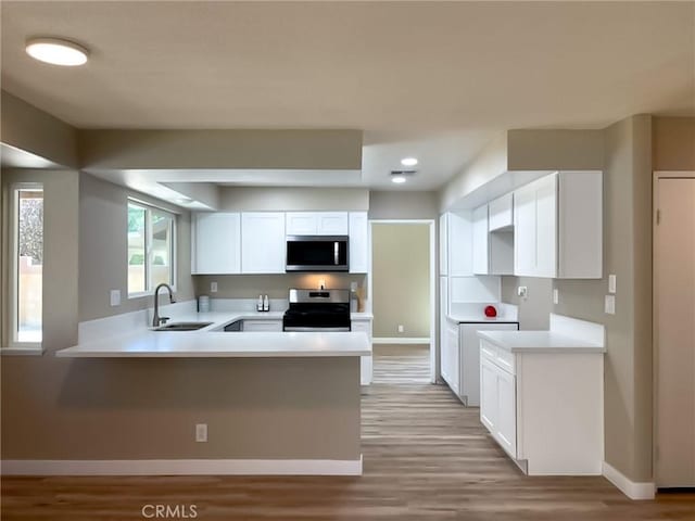 kitchen featuring stainless steel appliances, a sink, baseboards, a peninsula, and recessed lighting