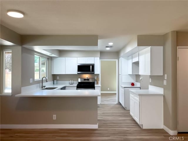 43856 Windsor Pl, Lancaster, CA 93536 - kitchen featuring appliances with stainless steel finishes, a peninsula, light wood-style flooring, white cabinetry, and light countertops