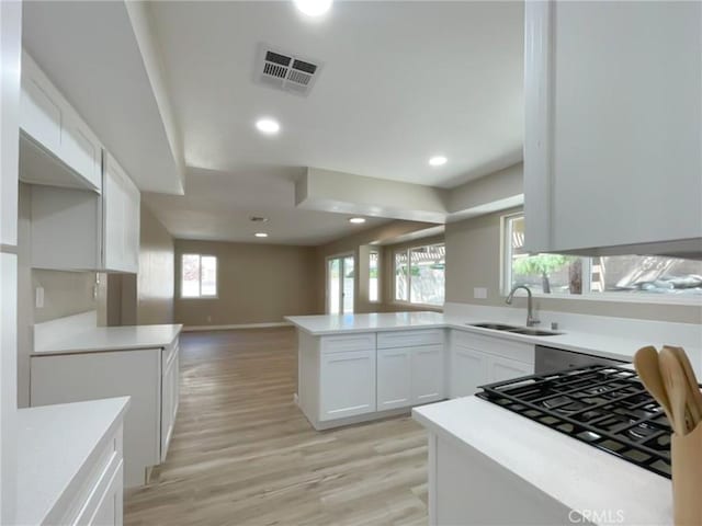 kitchen featuring a sink, open floor plan, light wood-type flooring, light countertops, and white cabinetry