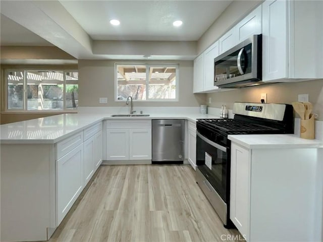 kitchen featuring appliances with stainless steel finishes, a sink, white cabinetry, light wood-style flooring, and recessed lighting