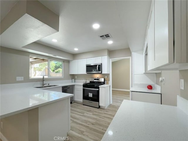 kitchen with stainless steel appliances, a sink, white cabinetry, light wood-style floors, and a peninsula