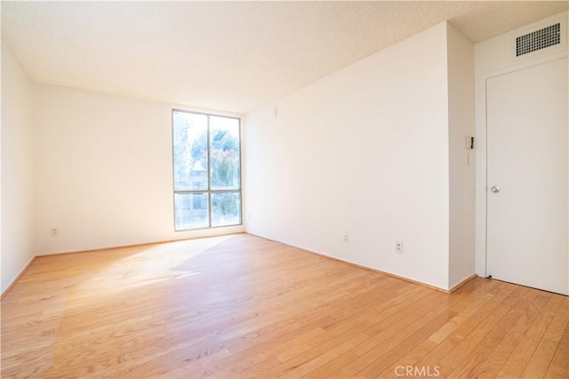 spare room featuring light wood finished floors, expansive windows, visible vents, and a textured ceiling