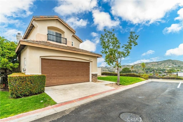 view of front of property with a balcony, driveway, fence, a garage, and stucco siding