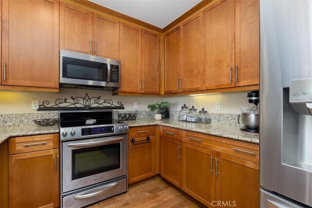 1021 Costa Pacifica Way Unit 2105, Oceanside, CA 92054 - kitchen featuring appliances with stainless steel finishes, light wood-style floors, brown cabinets, and light stone counters