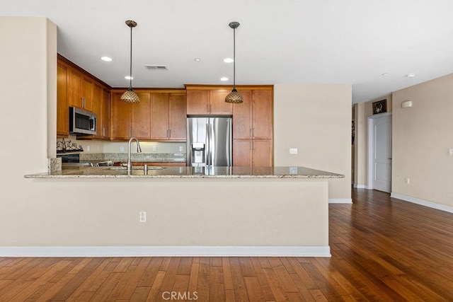 1021 Costa Pacifica Way Unit 2105, Oceanside, CA 92054 - kitchen with appliances with stainless steel finishes, light stone countertops, brown cabinetry, dark wood finished floors, and a peninsula