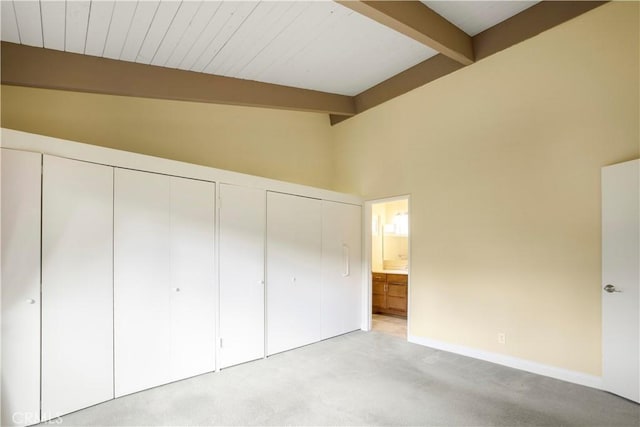 unfurnished bedroom featuring multiple closets, baseboards, ensuite bath, vaulted ceiling with beams, and light colored carpet