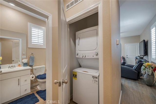 laundry room featuring stacked washer and clothes dryer, light wood-type flooring, a sink, visible vents, and laundry area