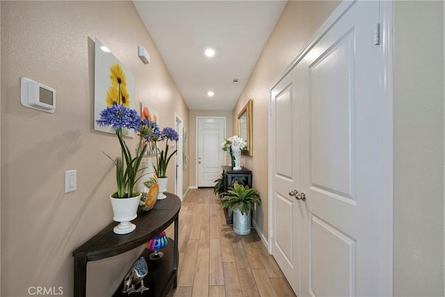 corridor featuring light wood-style flooring, baseboards, and recessed lighting