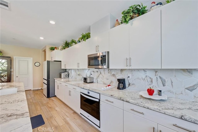 kitchen with white cabinetry, stainless steel appliances, decorative backsplash, visible vents, and light wood-style flooring